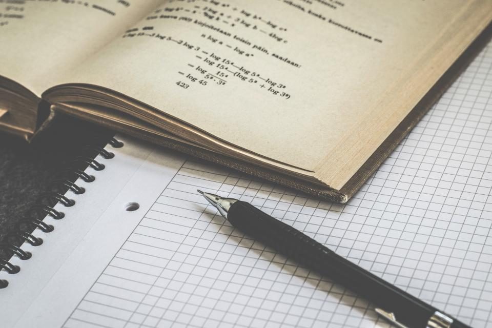 Otevřená učebnice matematiky a čtverečkovaný sešit s perem